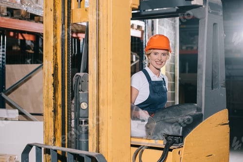 Preview: attractive workwoman sitting in forklift loader and smiling at camera