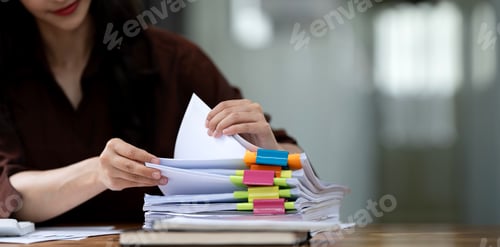 Preview: Businesswoman hands working in Stacks of paper files for searching and checking unfinished document