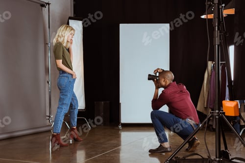 Preview: african american photographer taking photo of attractive model in studio