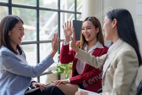 Preview: Asian female business colleagues giving high-five in a team meeting at office.