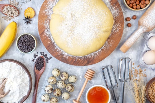 Preview: Top view of raw pastry flour on round board hazelnuts honey chocolates eggs banana flour on stained
