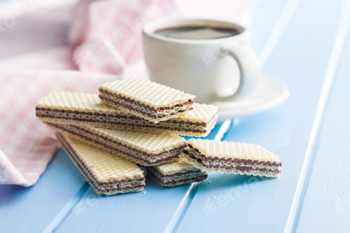 Preview: Sweet chocolate wafer and coffee cup on blue table.