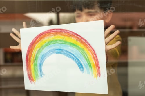Preview: Little kid holding a drawing of a rainbow through the window