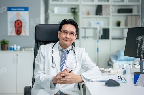 Preview: Portrait of Asian mature male doctor sitting on table in hospital office.