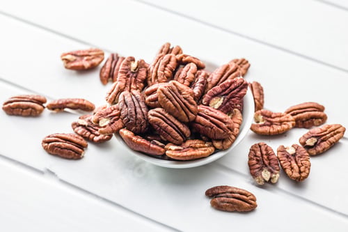 Preview: Peeled pecan nuts in bowl on white table.