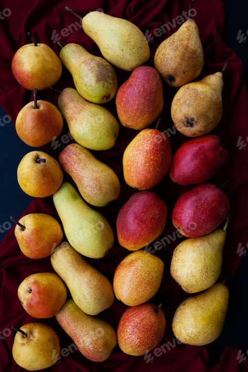 Preview: Yellow and red juicy fragrant pears lie on a cherry tablecloth on a black wooden background.