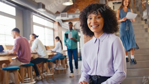 Preview: Portrait Of Smiling Businesswoman Working In Busy Open Plan Office With Colleagues In Background