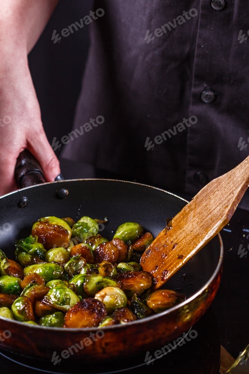 Preview: young woman fries Brussels sprouts on a frying pan