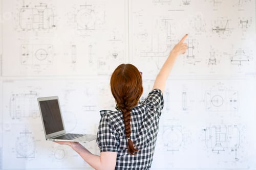 Preview: Young woman engineer shows something on the drawings and holds a laptop. the working process