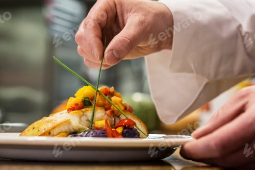 Preview: Hands of a chef dressing a plate of fish in a commercial kitchen,