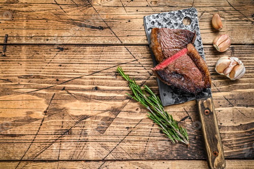 Preview: Grilled rump cap or brazilian picanha beef meat steak on a cleaver. wooden background.