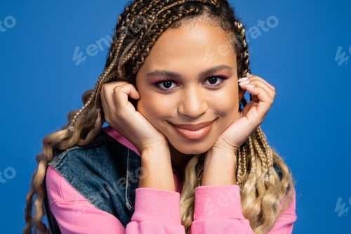 Preview: charming and happy african american woman looking at camera on blue background, fashion and beauty
