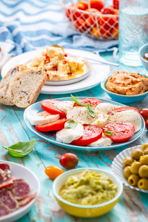 Preview: Picnic table with assorted appertizers, raw vegetables, cheese, dips, baguette and pastrami