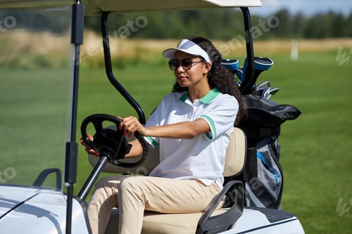 Preview: Young black woman driving golf cart on green field in sunlight