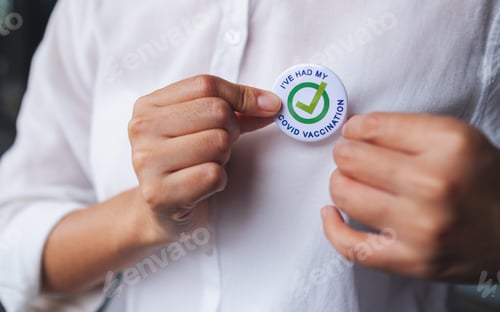 Preview: Closeup image of a woman putting Covid-19 vaccinated sign brooch on shirt