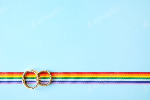 Preview: Top view of wedding rings and rainbow ribbon on color background, space for text. Gay symbol