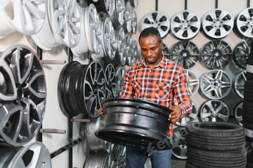 Preview: African american Car mechanic holding car rims ready to mount the wheels in workshop