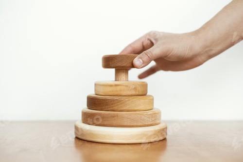 Preview: Hand holding natural wooden pyramid ring on table. Eco friendly plastic free modern toys. Montessori