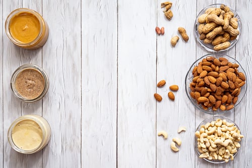 Preview: Jars of Almond, Cashew and Peanut Butter on a White Wooden Table.