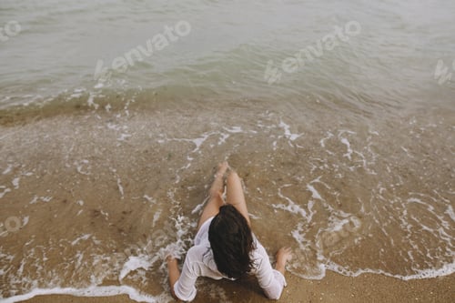 Vorschau: Junge Frau im nassen weißen Hemd liegt am Strand in plätschernden Wellen