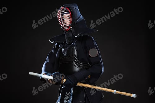 Preview: Kendo fighter in helmet holding bamboo sword and looking away on black