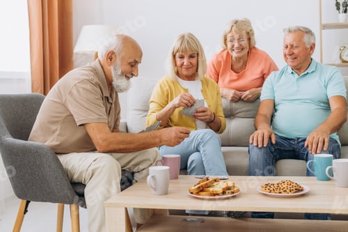 Preview: Group of senior people laughing while relaxing at home and playing cards.