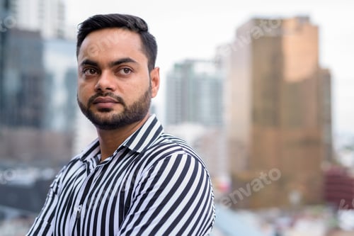 Preview: Young bearded Indian businessman against view of the city
