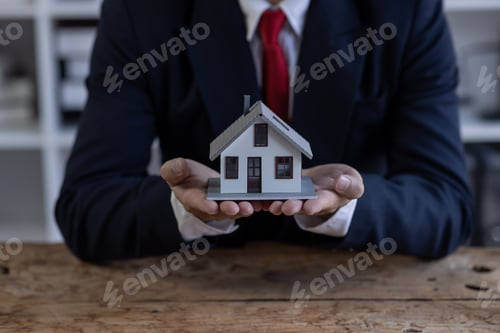 Preview: Mortgage concept. Small toy house in business man hand buy or sell real estate Financial agent compl