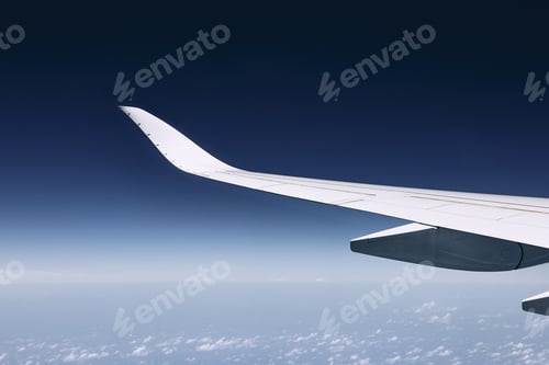 Preview: Wing of modern airplane flying over clouds against dark blue sky.