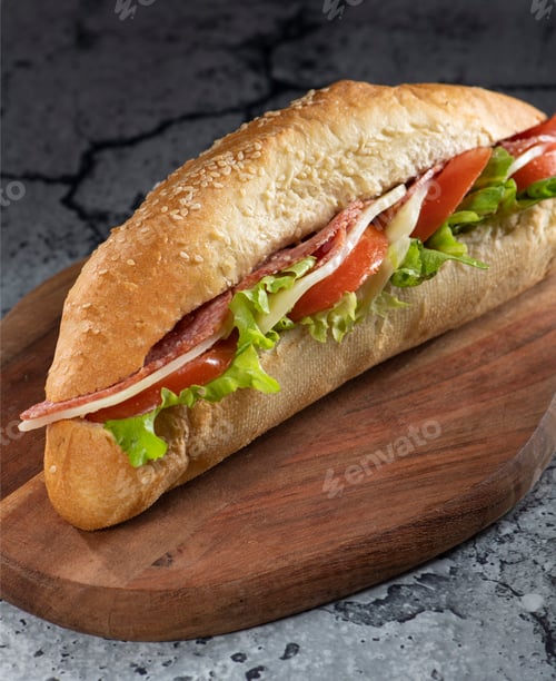 Preview: One baguette sandwich on a cutting board with tomatoes, cheddar, salami, lettuce, mayonnaise