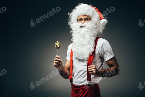 Preview: smiling santa claus in eyeglasses standing with colorful lollipop isolated on grey background