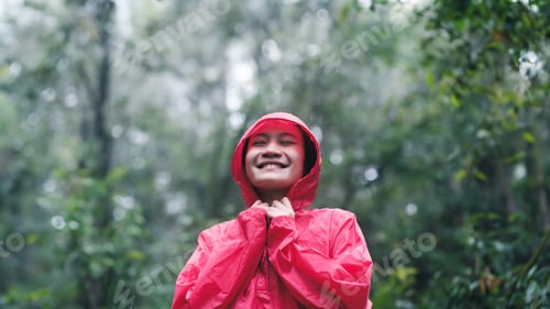 Preview: Smiling woman in red raincoat enjoying the forest