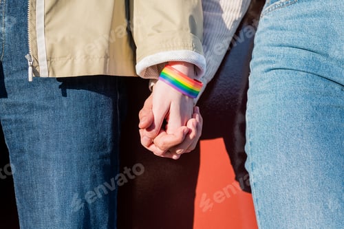 Preview: linked hands of two women with a rainbow bracelet