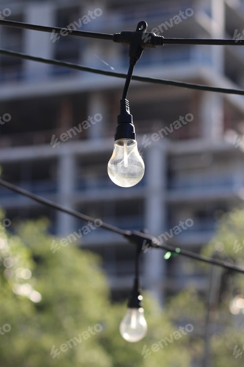 Preview: Selective focus shot of a light bulb hanging from string lights in a city