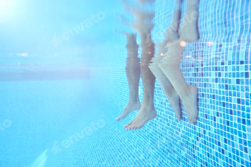 Preview: Underwater Shot Of Couples Legs As They Sit On Edge Of Swimming Pool On Vacation