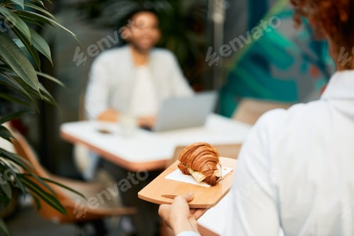 Preview: Close-up of waitress serving croissant to her customer in a cafe.