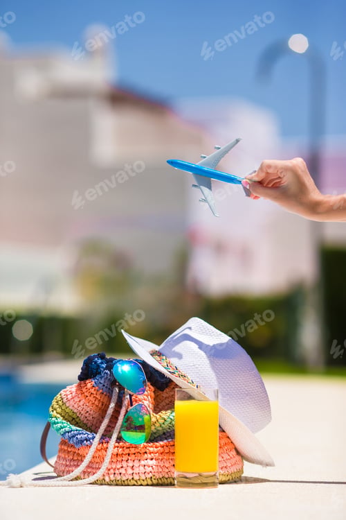 Preview: Colorful beach bag, glass of juice, straw hat and airplane model in female hand on summer vacation