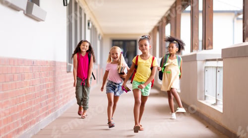 Preview: Full length of happy multiracial elementary schoolgirls walking in corridor