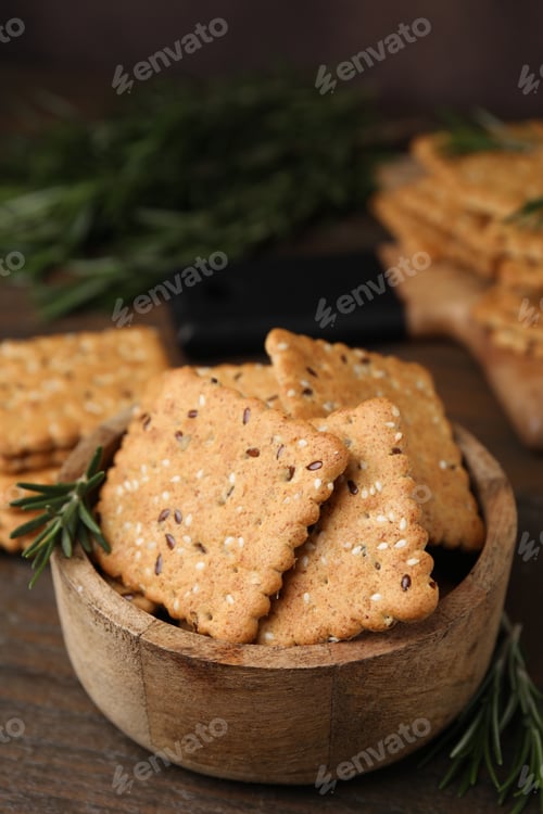 Preview: Cereal crackers with flax, sesame seeds and rosemary in bowl on wooden table, closeup