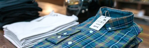 Preview: Close up of label with price and size over a blue plaid shirt on industrial style store