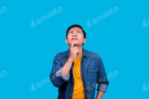 Preview: Portrait Of Young Asian Male Thinking With Hand On Chin Isolated On Blue Background