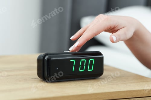 Preview: Woman turning off digital alarm clock on bedside table indoors, closeup