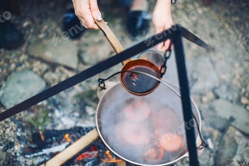 Preview: From above traditional mulled wine with slices of orange preparing in pot over burning logs