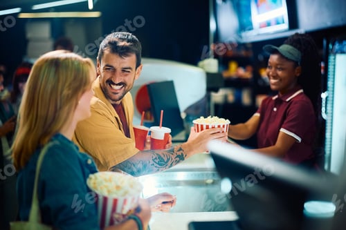 Preview: Happy couple buying popcorn and soda at concession stand in movie theater.