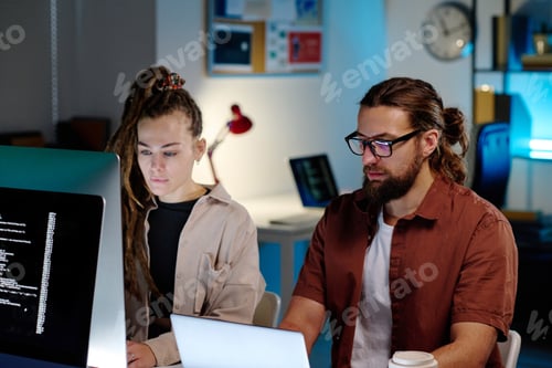 Preview: Two young serious coworkers sitting in dark office at night and decoding data