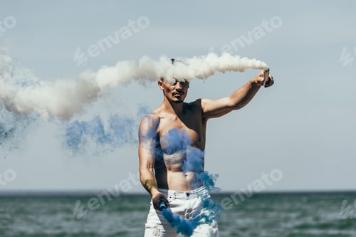 Preview: attractive man holding blue and white smoke sticks in front of sea