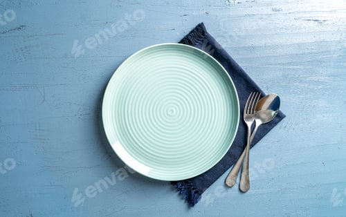 Preview: Top view of white plate with spoon and fork on a blue wood table