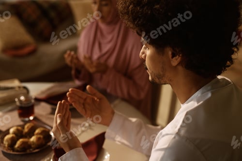 Preview: Close up of religious Arab couple praying at dining table.