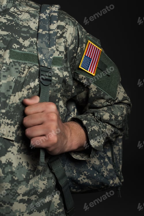 Preview: cropped view of American serviceman in military uniform with flag standing with backpack isolated