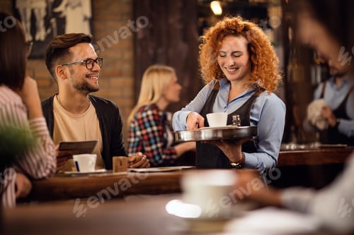 Preview: Young redhead waitress serving coffee to her guests in a cafe,